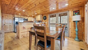 A wooden cabin interior with a dining area, kitchen, and a large window.