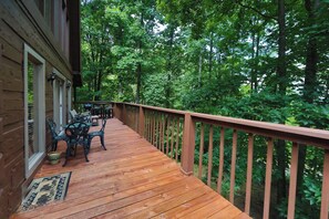 A wooden deck with outdoor furniture, surrounded by dense forest. - Secluded | Pigeon Forge | Pool Table | Arcade | Pet Friendly | Hot Tub | WiFi (PIGEON FORGE)