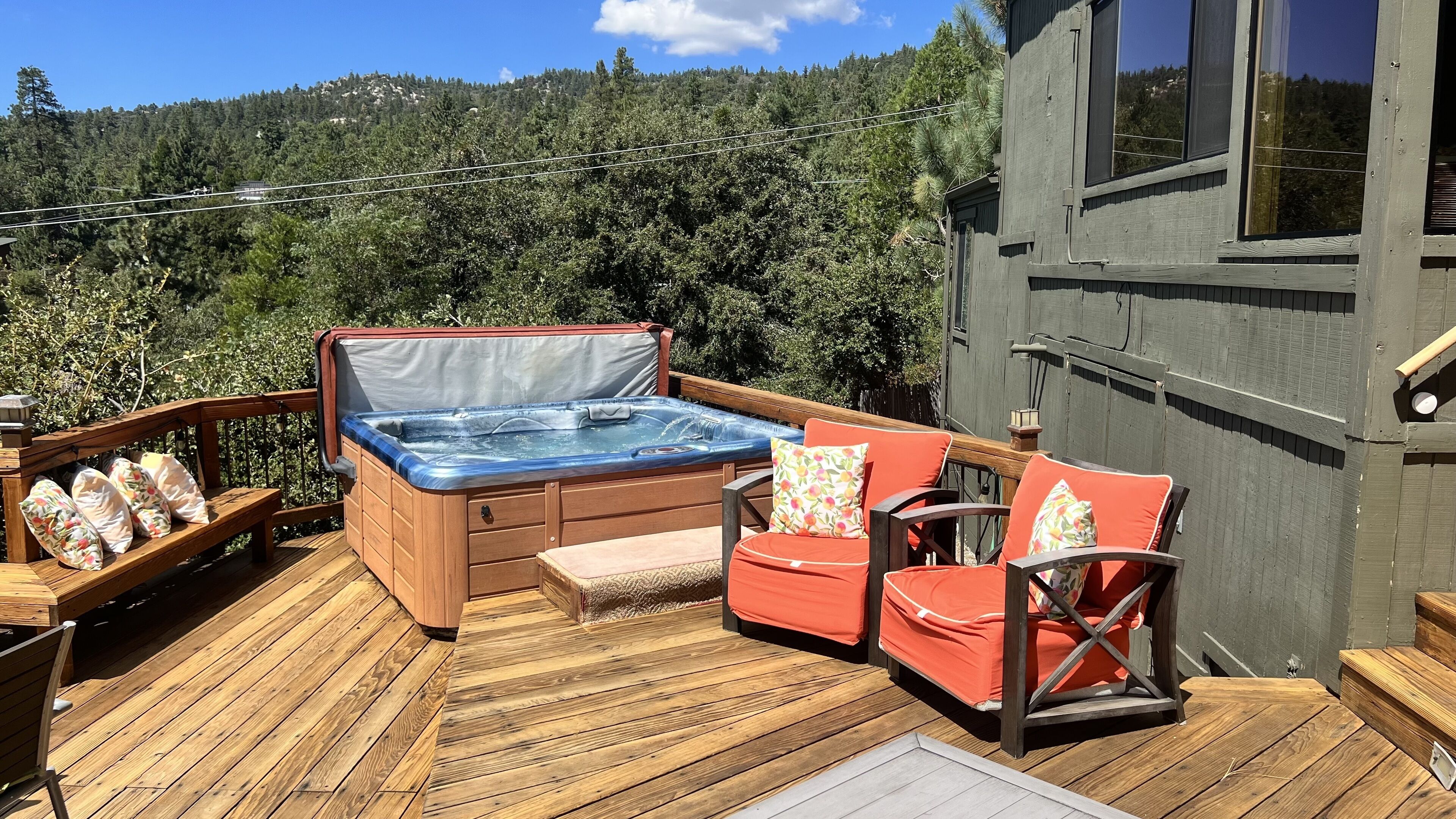 Eine Holzterrasse mit Whirlpool, zwei roten Stühlen und einem Holztisch.