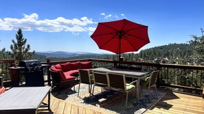 A deck with a red umbrella, a grill, a red sofa, and a table with chairs.