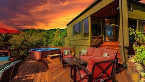 Eine Holzterrasse mit Sitzgelegenheiten im Freien, einem Whirlpool und Blick auf einen bewaldeten Bereich.