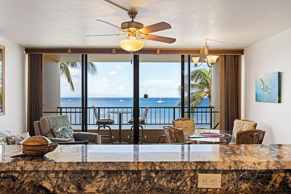 A hotel room with a balcony, a ceiling fan, and a view of the ocean.