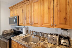 Una cocina con armarios de madera, microondas de acero inoxidable, tostadora, licuadora, fregadero y estufa.