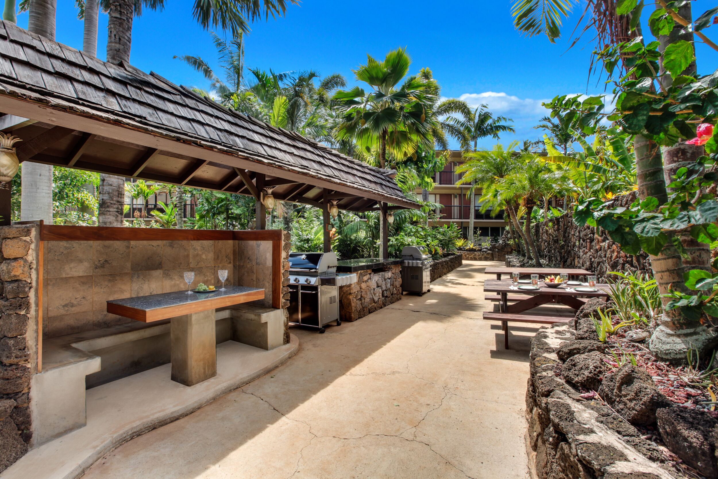 Un patio al aire libre con una parrilla, asientos y una zona cubierta con un muro de piedra.