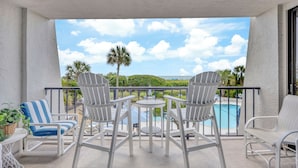 Un balcone con sedie e tavolo bianchi, con vista su una piscina e palme.
