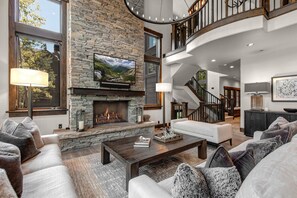 A modern living room with a stone fireplace, a large flat-screen TV, and a staircase leading to an upper level.