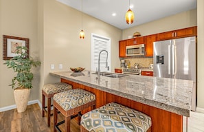A kitchen with a central island, stainless steel appliances, and a hanging pendant light. - Maui Resort Rentals: Honua Kai Konea 145, Upgraded Groundfloor Interior, Huge Lawn Area, Steps to Pools/Beach/BBQs! (Lahaina)