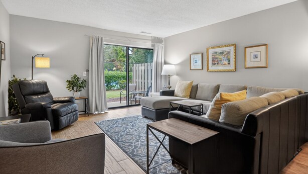 Un salon moderne comprenant un canapé, des fauteuils, une table basse et un lampadaire. Une porte-fenêtre coulissante donne accès à un jardin.