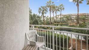 A balcony with a white chair and a view of palm trees and a building in the background.
