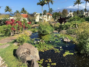 Un jardín tranquilo con un estanque, abundante vegetación y palmeras.
