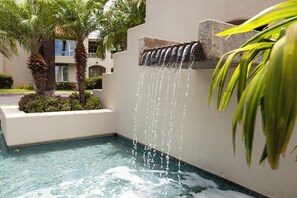A water feature with cascading water, palm trees, and a pool with mosaic tiles.
