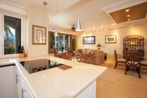 A modern kitchen with an island, dining area with wicker furniture, and a living room with a sofa and chairs.