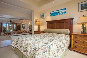 Un dormitorio con una cama grande, cabecera de madera y colcha estampada con flores. Hay una mesita de noche con lámpara, un aparador y un cuadro en la pared.