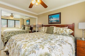 A bedroom with a large bed, a ceiling fan, a nightstand with a lamp, a mirror, and a framed picture on the wall.