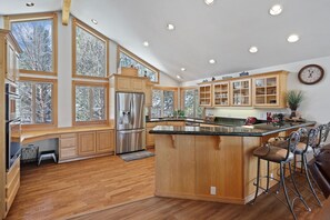 A spacious kitchen with wooden cabinets, a stainless steel refrigerator, and a large island with bar stools. - 2 Sarazen - Golf Course Views, Hot Tub, SHARC Passes, Perfect for a Family Getaway (Sunriver)