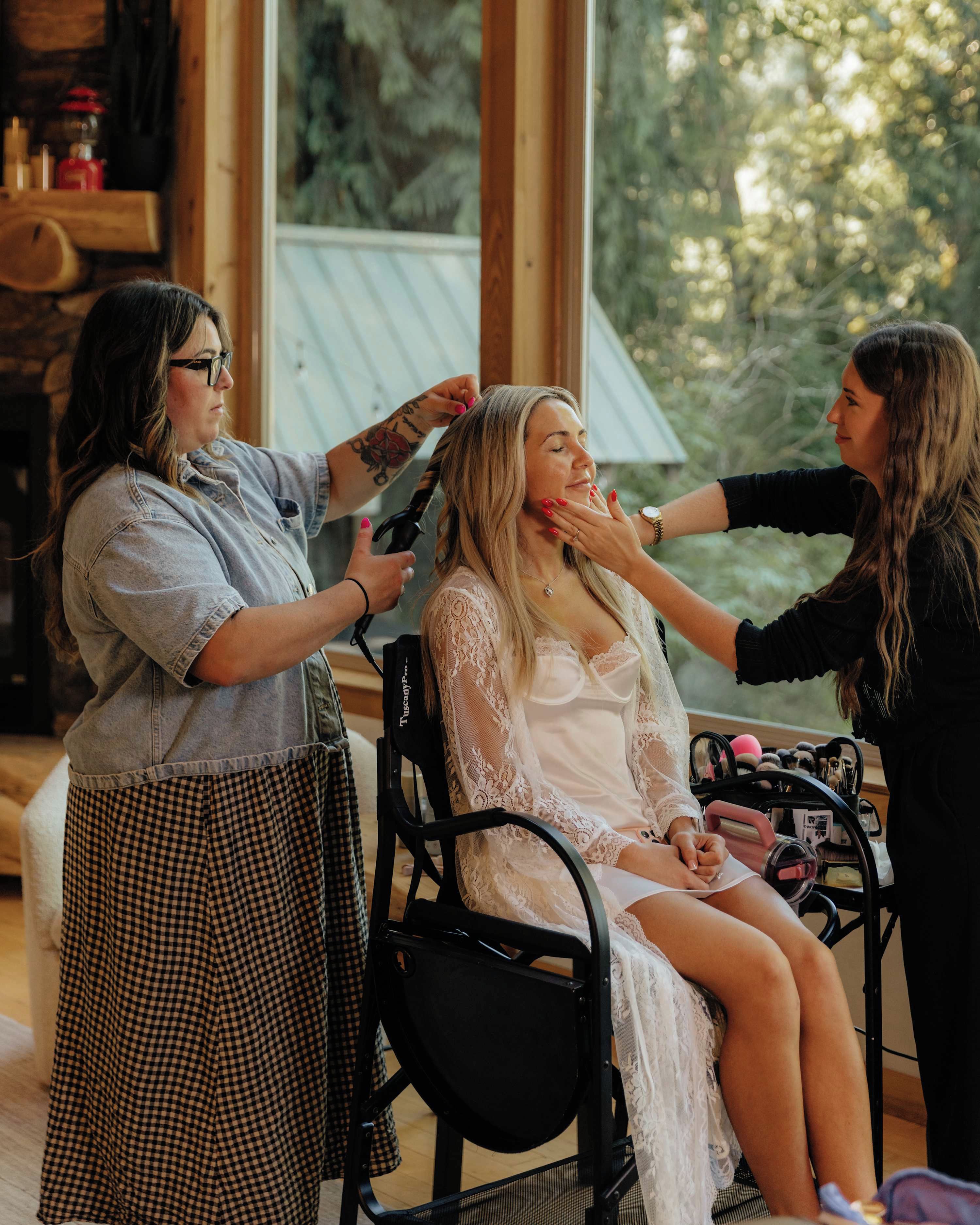 A person seated in a chair with a makeup artist applying makeup.