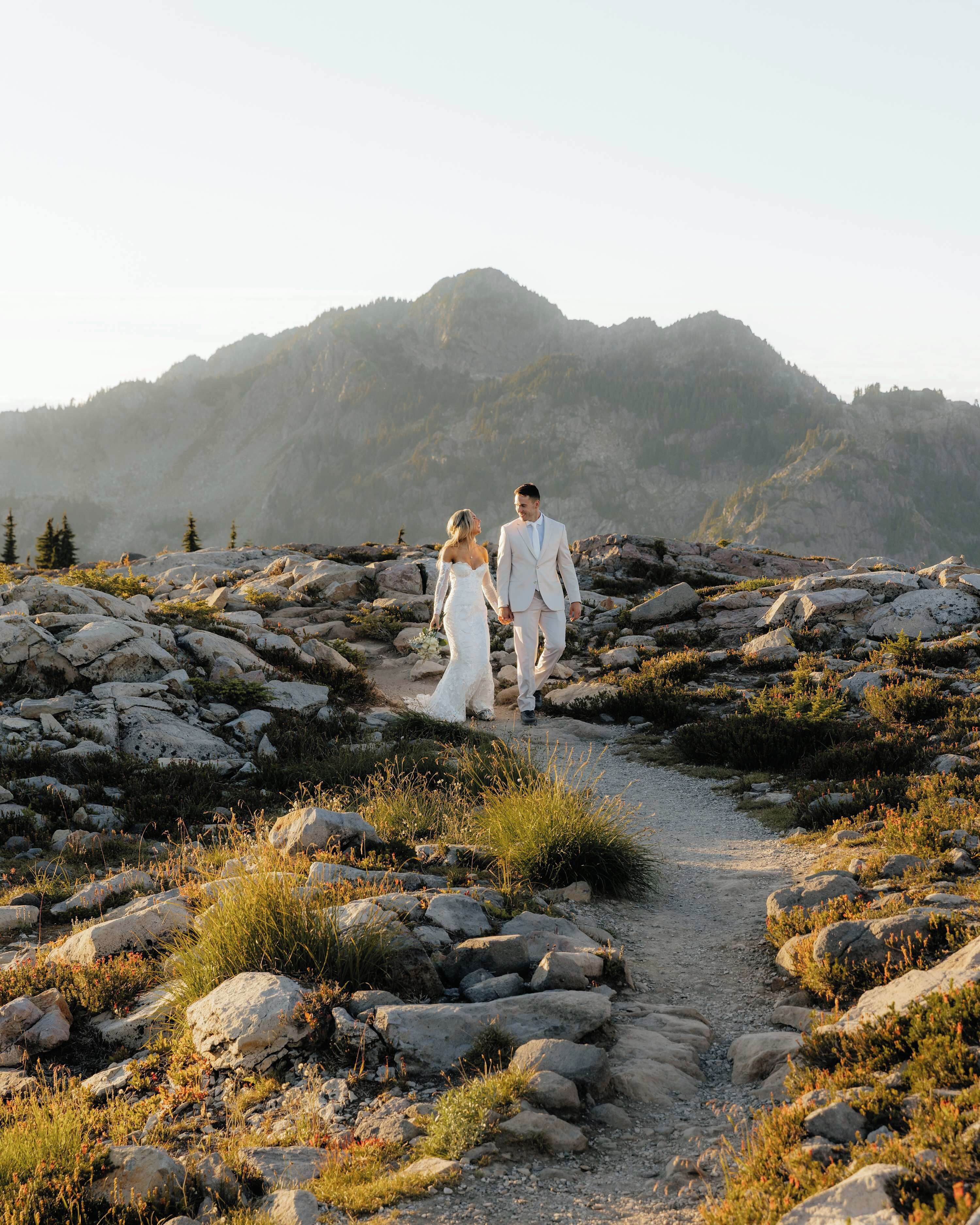 A couple walking on a rocky path with mountains in the background.