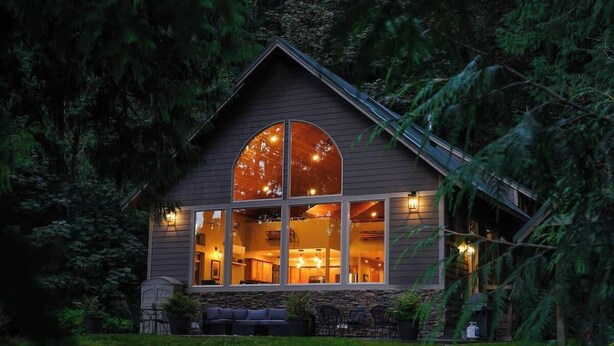 Une cabane confortable avec une grande fenêtre, des fondations en pierre et un intérieur bien éclairé.