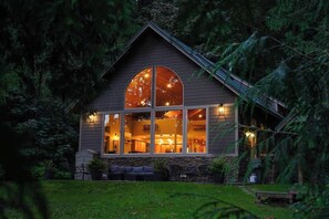A cozy cabin with a large window, a stone foundation, and a well-lit interior.