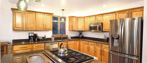 A modern kitchen with wooden cabinets, stainless steel appliances, and a granite countertop.