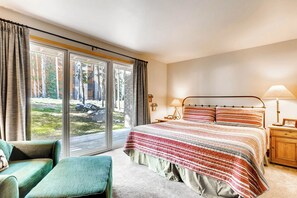 A bedroom with a large window, a bed with striped bedding, a nightstand, a lamp, and a chair.