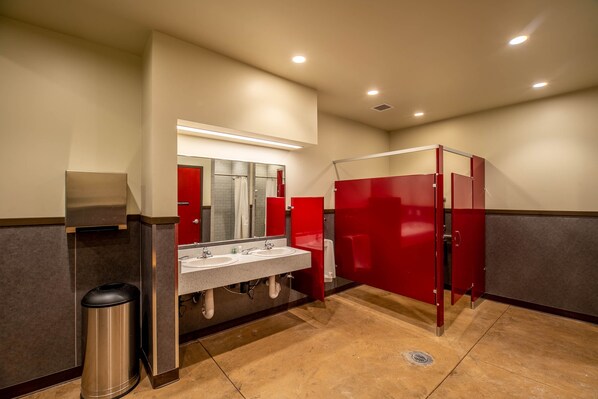A public restroom with two sinks, a trash can, and red stalls.