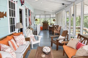 A covered porch with wooden furniture, a dining table, and a view of greenery. - Cozy, rustic home on Sullivan's Island near beach; great screen porch! (Sullivan's Island)
