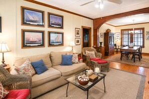 A living room with a sofa, armchairs, a glass coffee table, and framed maritime paintings on the wall. - Cozy, rustic home on Sullivan's Island near beach; great screen porch! (Sullivan's Island)