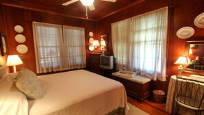 Una camera d'albergo con un grande letto, due finestre con tende, una televisione, una scrivania con lampada e una sedia.