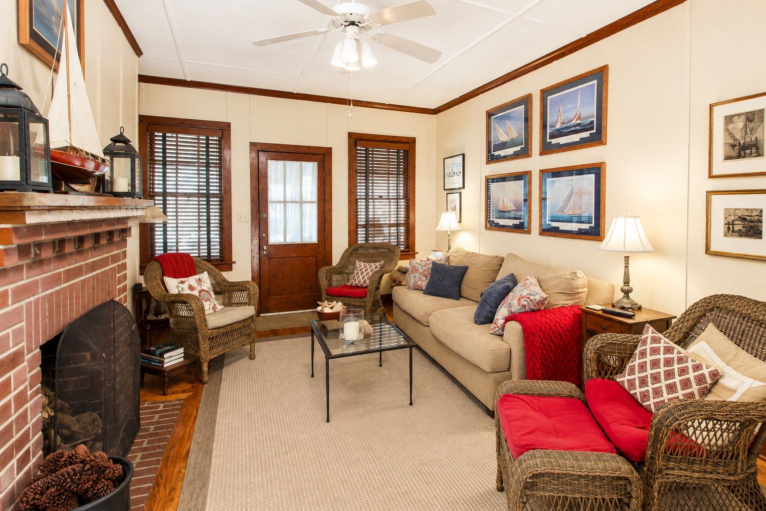A cozy living room with a fireplace, wicker furniture, and nautical-themed wall art.