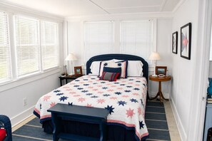 A bedroom with a bed, bedside tables, a bench, and a window with blinds.