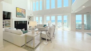 Ein großzügiges Wohnzimmer mit großem Fernseher, bequemen Sitzgelegenheiten und einem Balkon mit Meerblick.