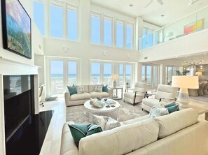Uma sala de estar ampla com uma grande janela com vista para o oceano, uma TV de tela plana e um alto teto com claraboia.