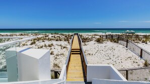 Ein hölzerner Steg führt zu einem Strand, der von blauem Himmel überdacht wird.