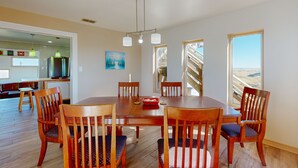 A dining area with a wooden table and chairs, a painting on the wall, and a view of a staircase leading to a balcony. - Views of the Gulf, Ample Parking for Boat and Cars (Port Aransas)