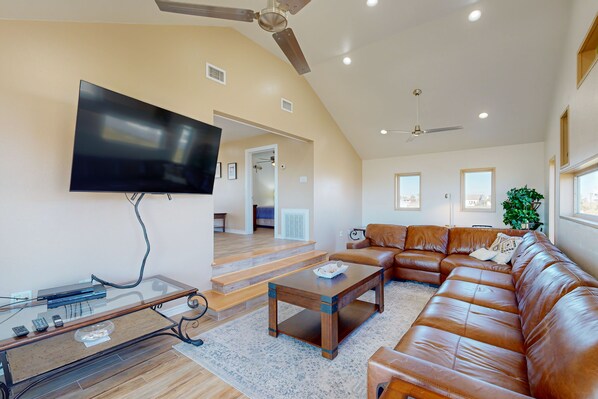 A spacious living room with a large leather sofa, a glass coffee table, and a flat-screen TV mounted on the wall.