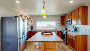 A modern kitchen with wooden cabinets, a stainless steel refrigerator, a large island with stools, and a hanging pendant light. - Views of the Gulf, Ample Parking for Boat and Cars (Port Aransas)