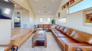 A spacious living room with a large brown leather sectional sofa, a wooden coffee table, and a ceiling fan. - Views of the Gulf, Ample Parking for Boat and Cars (Port Aransas)