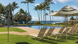A poolside area with lounge chairs and umbrellas, surrounded by palm trees and a view of the ocean. - Manualoha 603 Ground Floor By Suite Paradise (Koloa)