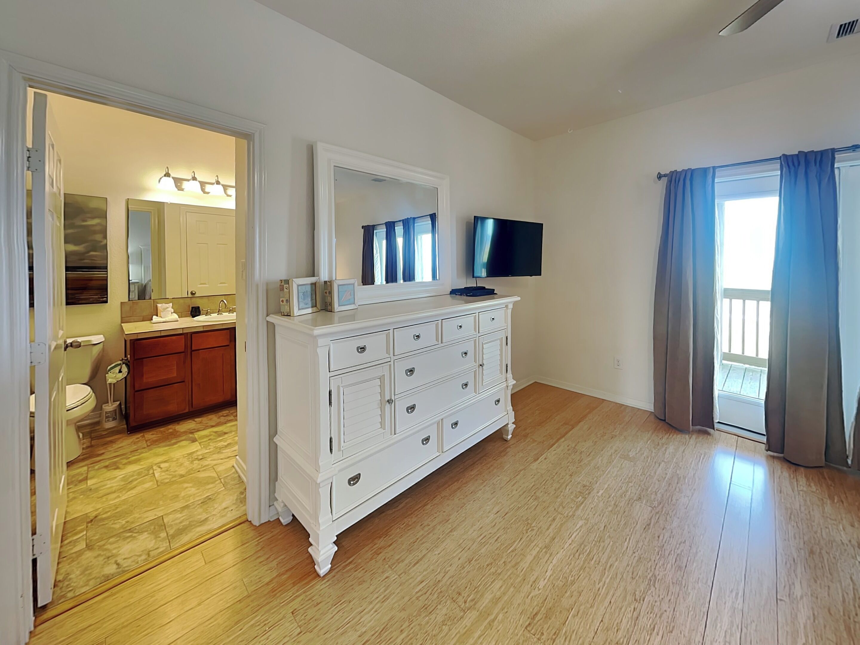 Une pièce avec une commode blanche, un téléviseur, une salle de bain avec un lavabo et des toilettes, et une vue sur l’extérieur par une fenêtre.