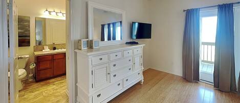 Une pièce avec une commode blanche, un téléviseur, une salle de bain avec un lavabo et des toilettes, et une vue sur l’extérieur par une fenêtre.