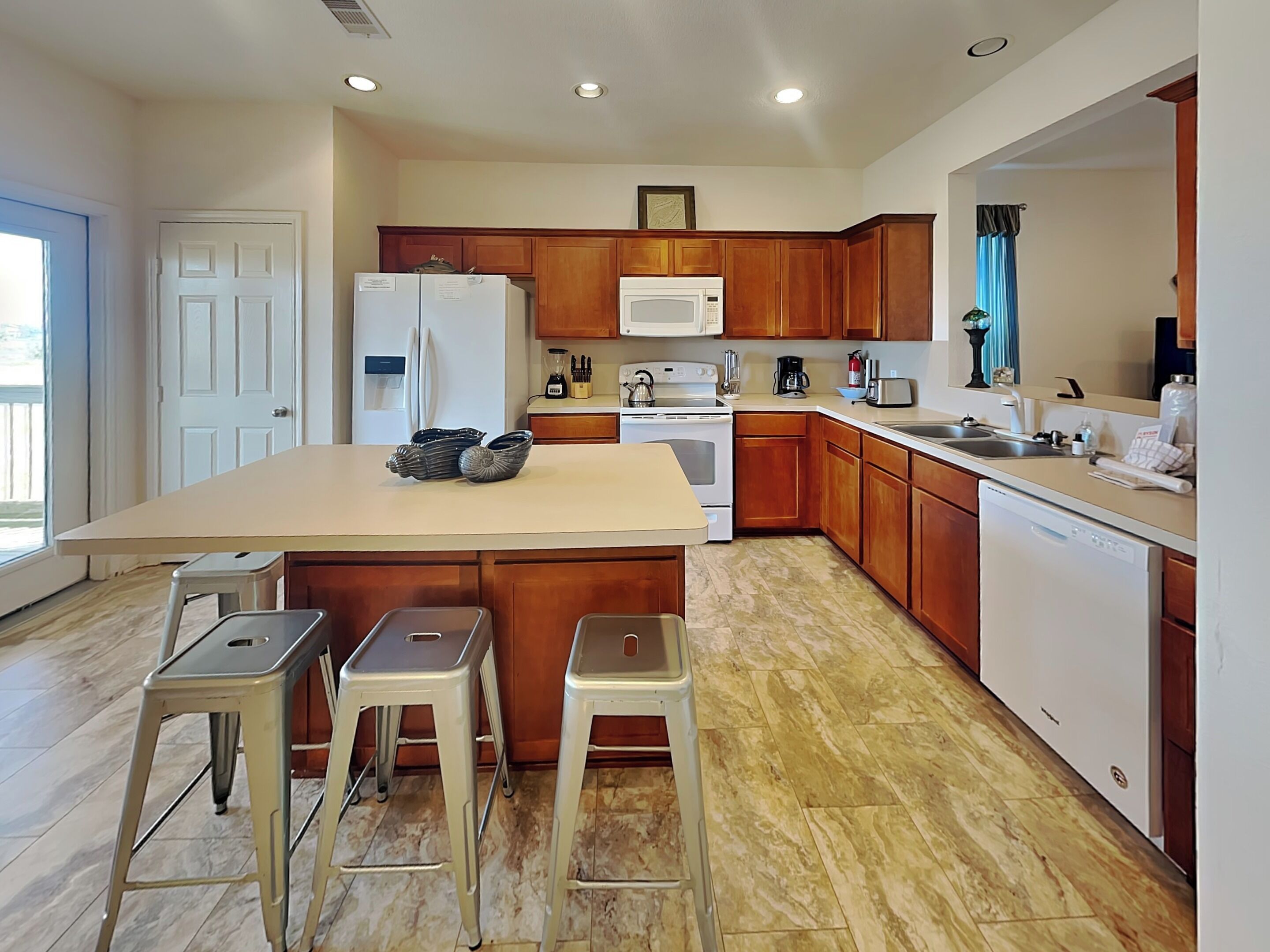 A modern kitchen with wooden cabinets, a central island with stools, a refrigerator, microwave, stove, and a dishwasher.