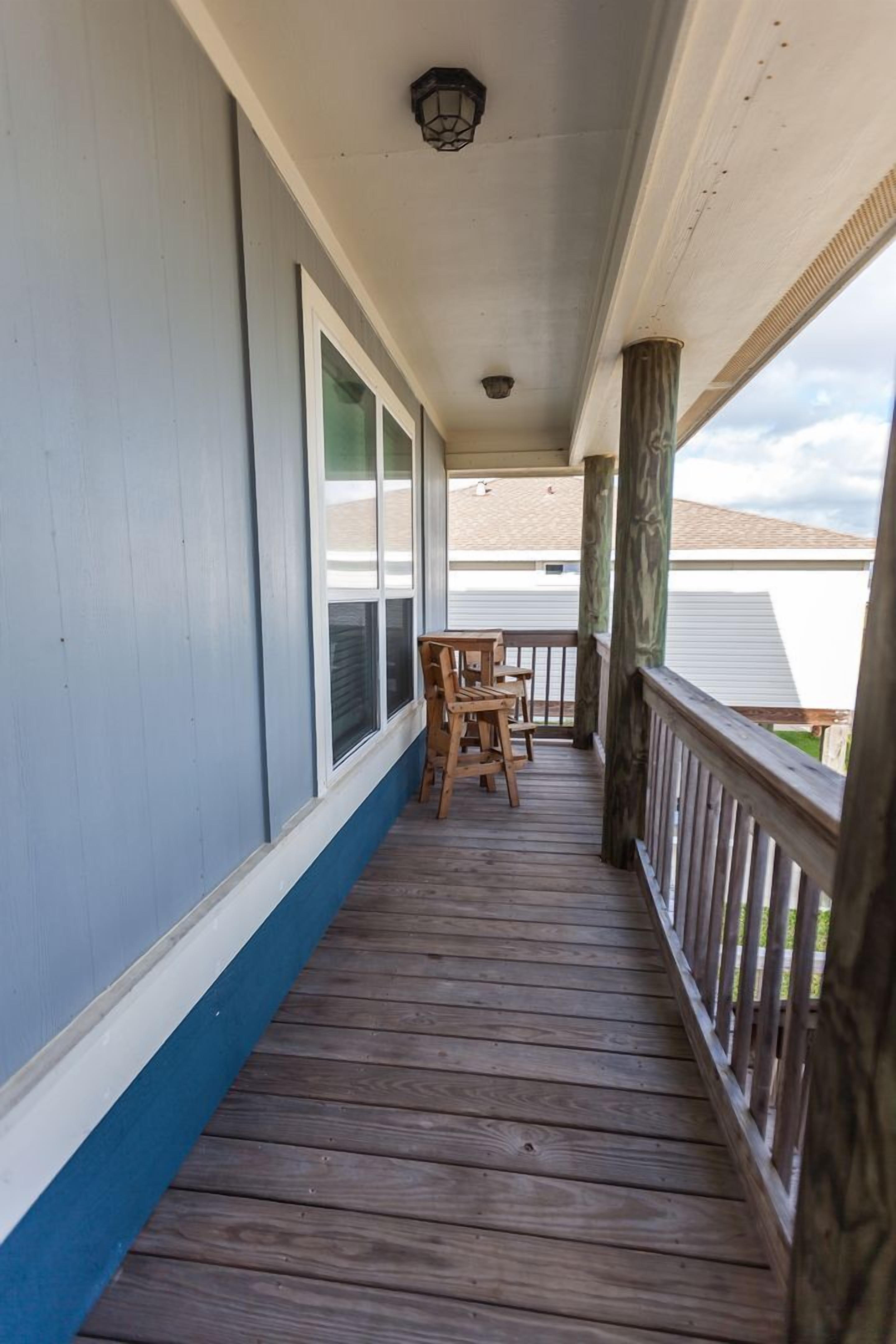 A covered porch with a wooden floor, a railing, and two wooden chairs.