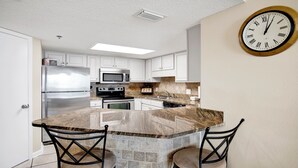 A modern kitchen with white cabinets, stainless steel appliances, a granite countertop, and a wall-mounted clock. - Beautifully Updated Phoenix VI 2BR 4th Floor Condo!! (Orange Beach)