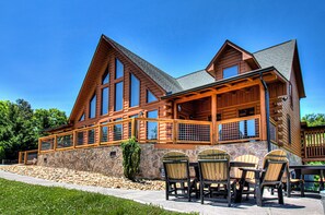 A log cabin with a stone foundation, large windows, and a covered patio with outdoor seating.