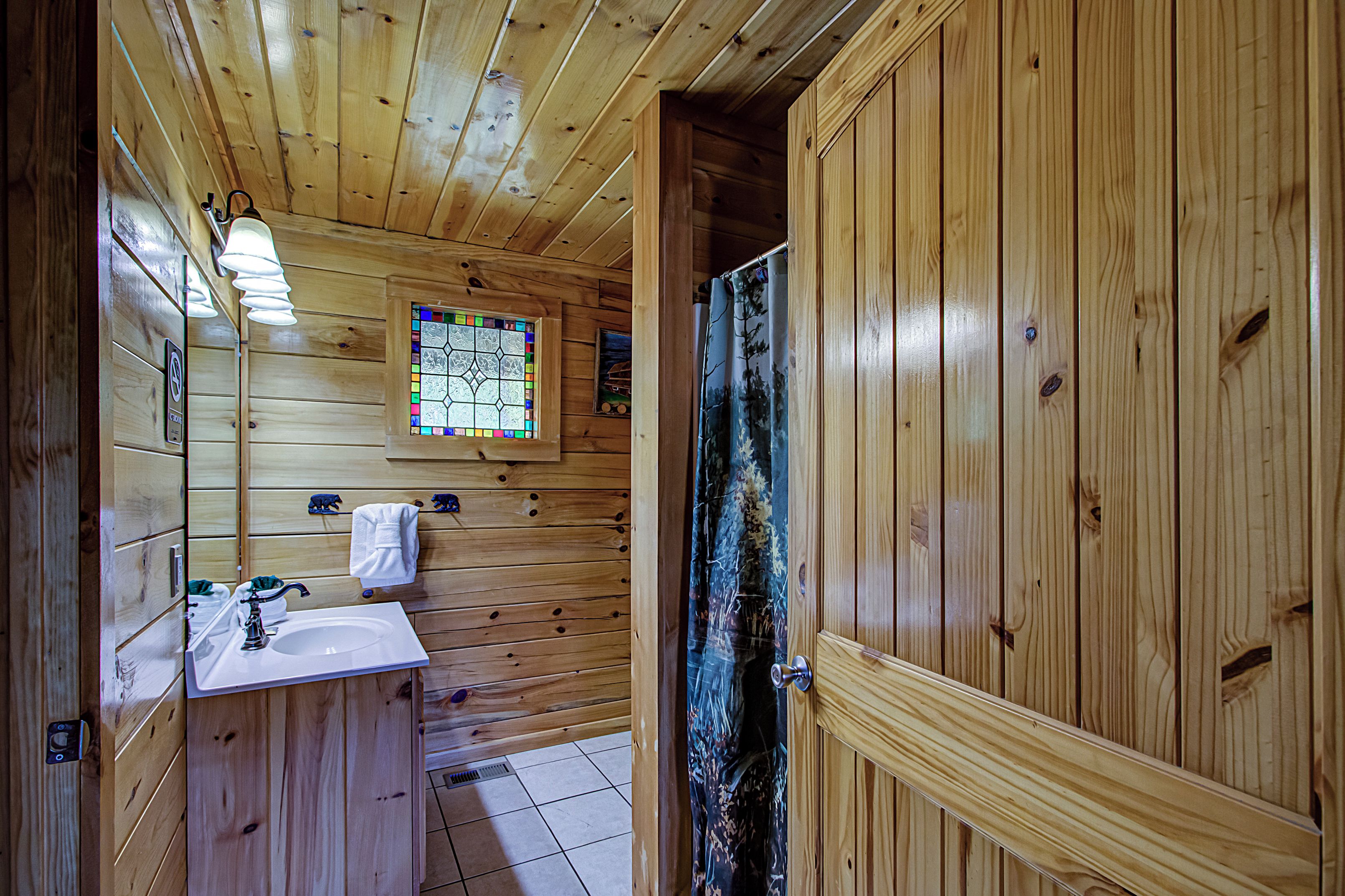 A wooden cabin bathroom with a sink, mirror, and a stained glass window.