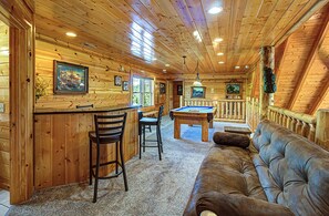 A wooden cabin interior with a pool table, bar area, and seating.