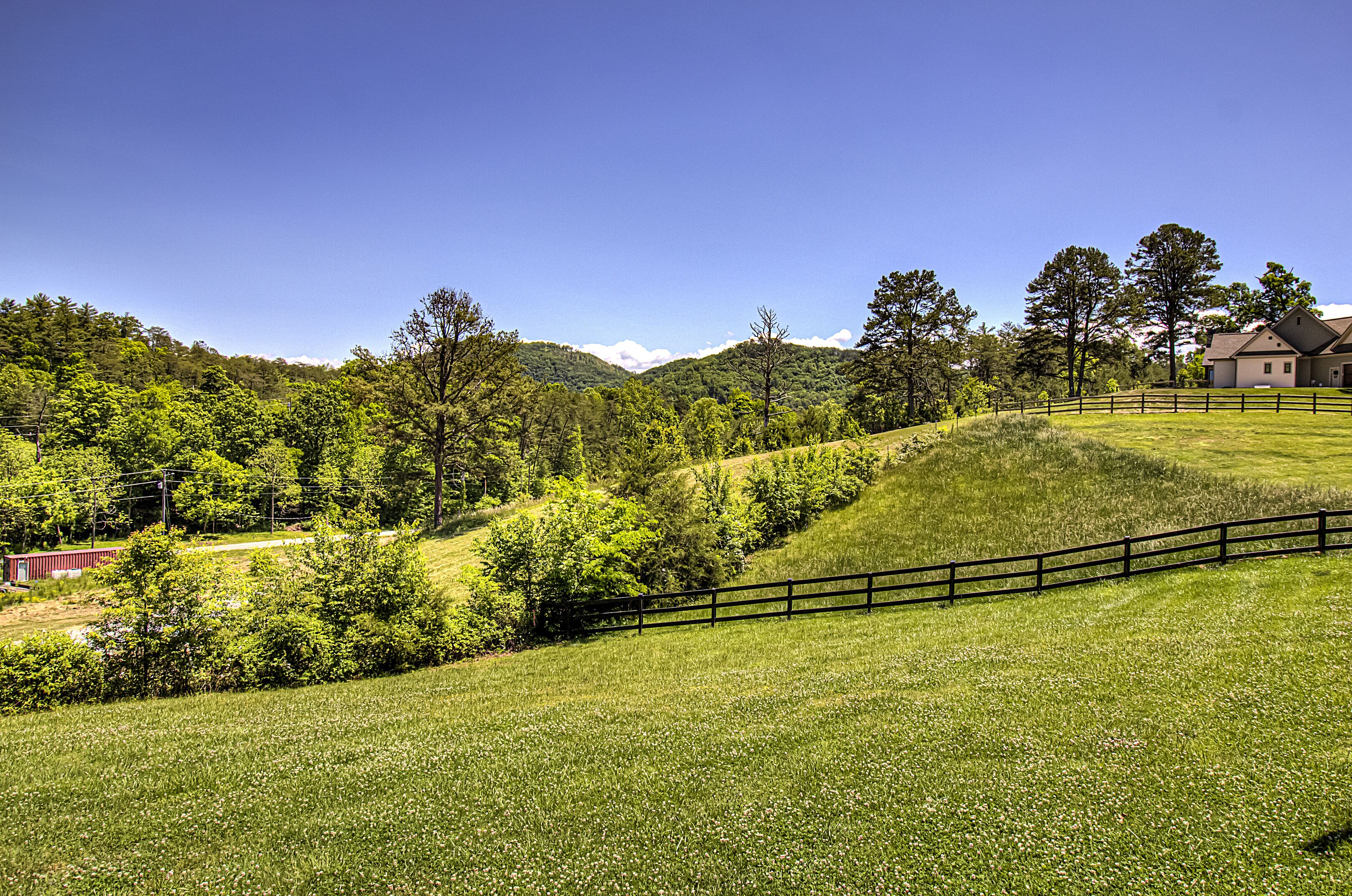 A rural landscape with a fenced property, a house, and a hilly backdrop.