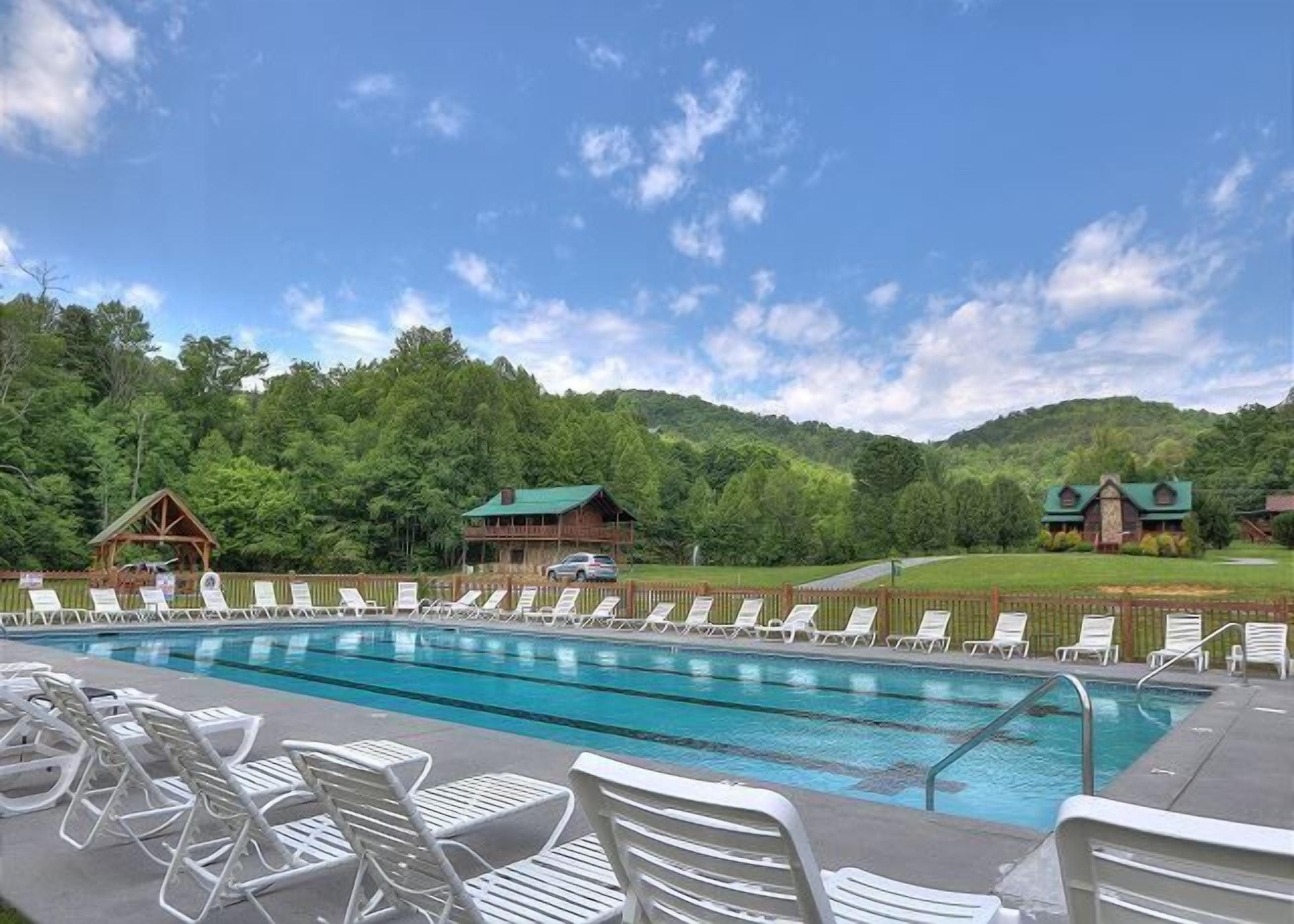 Une piscine avec des chaises longues et un chalet en bois situé dans une zone boisée.