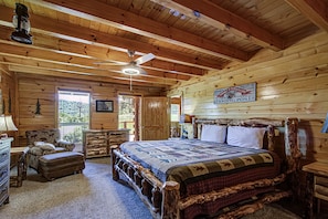 A log cabin bedroom with a wooden bed, a ceiling fan, and a sign for 'Schnitzel's Furniture Trading Post'. - Luxury Cabin w/Pool Table, Fire Pit, and Hot Tub (SEVIERVILLE)